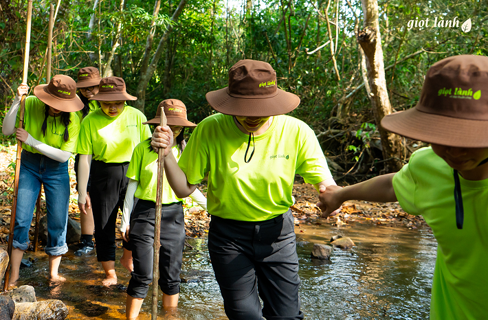 Đoàn thành viên Giọt Lành nắm tay nhau băng qua con suối nhỏ